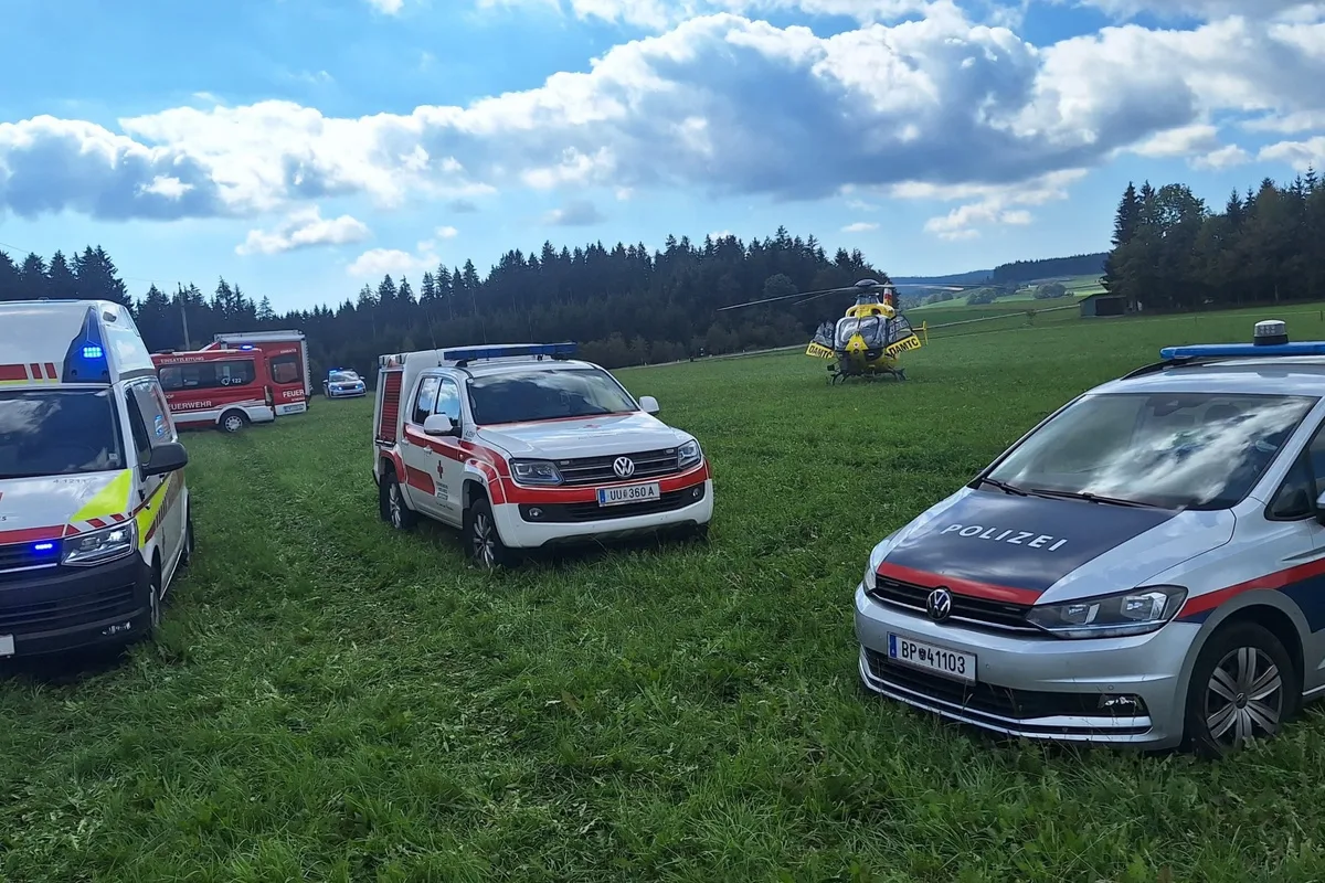 Zahlreiche Einsatzfahrzeuge, einschließlich Polizei und Rettung, sowie ein gelber Hubschrauber auf einer Wiese in ländlicher Umgebung.