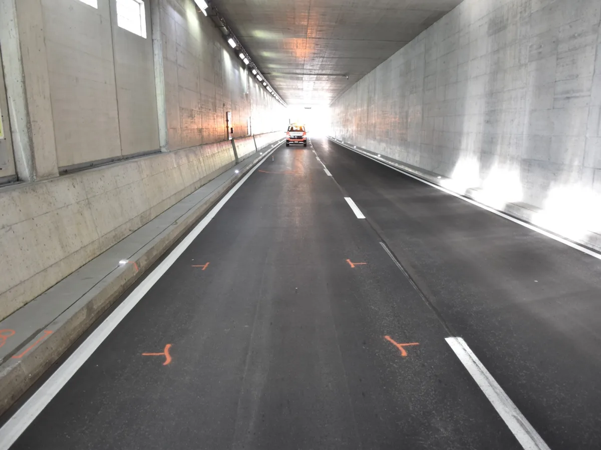 Ein leeres, gut beleuchtetes Tunnelinnere führt zu einem hellen Ausgang, wo ein Fahrzeug sichtbar ist.