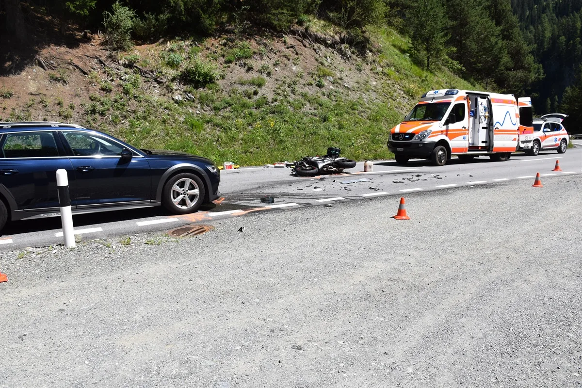 Ein beschädigtes Motorrad liegt auf einer Landstraße, daneben ein Auto und ein Krankenwagen mit geöffneten Türen. Verkehrshütchen sind aufgestellt.