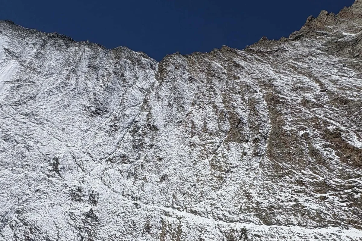 Nahaufnahme eines schneebedeckten, felsigen Berggrats unter einem klaren, blauen Himmel.