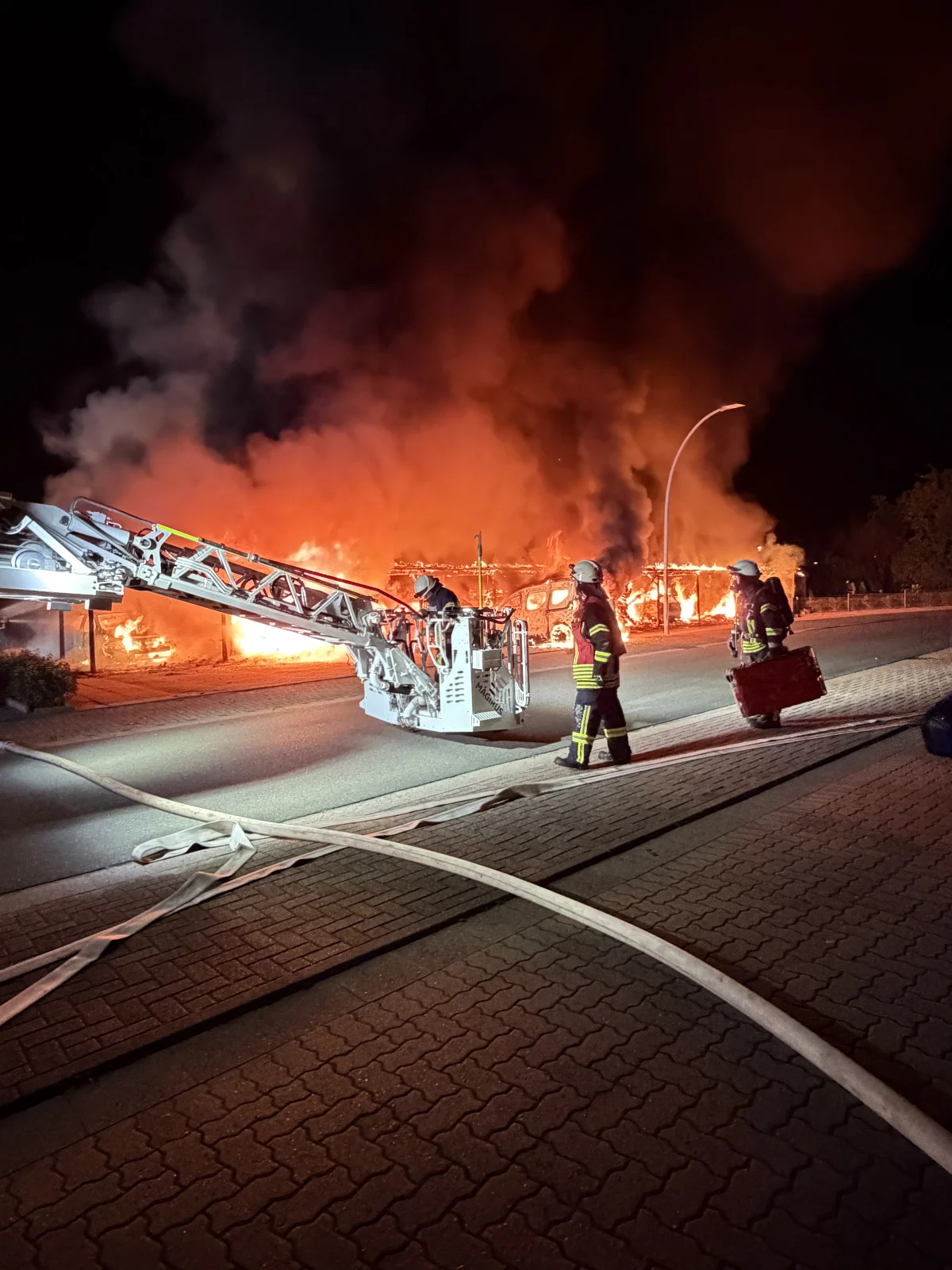 Mehrere Feuerwehrmänner führen nachts Löscharbeiten bei einem großen Brand durch. Eine Drehleiter ist im Einsatz.