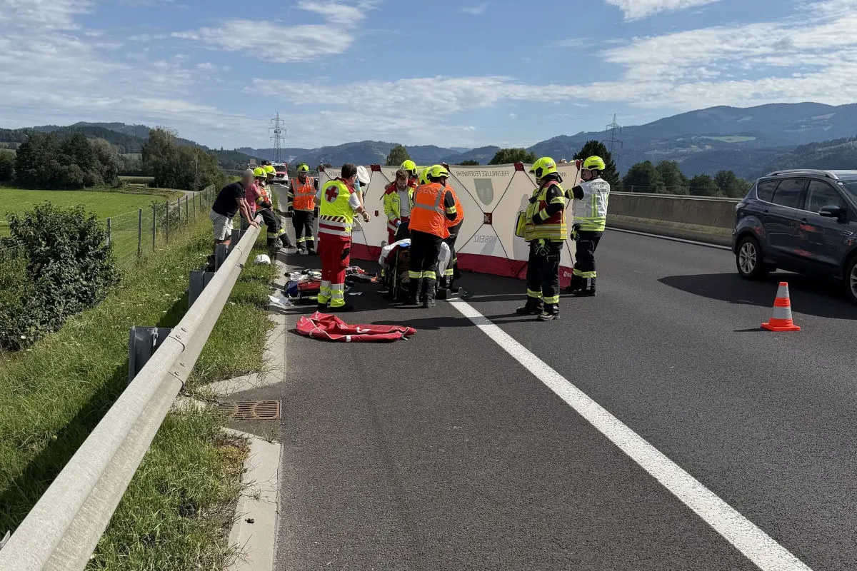 Mehrere Rettungskräfte in Warnwesten arbeiten auf einer Autobahn hinter einem Sichtschutz. Daneben steht ein Auto.