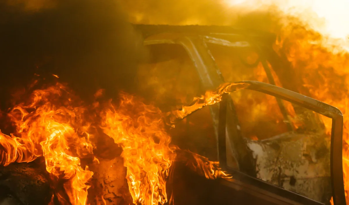 Das Bild zeigt ein Auto, dessen Innenraum in extremen Flammen steht, während die Tür geöffnet ist.