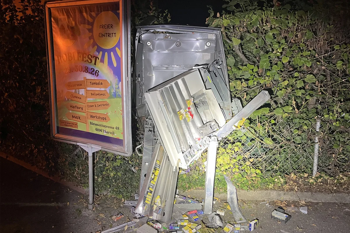 Ein Zigarettenautomat steht stark beschädigt am Straßenrand. Daneben liegen zahlreiche Zigarettenpackungen verstreut.