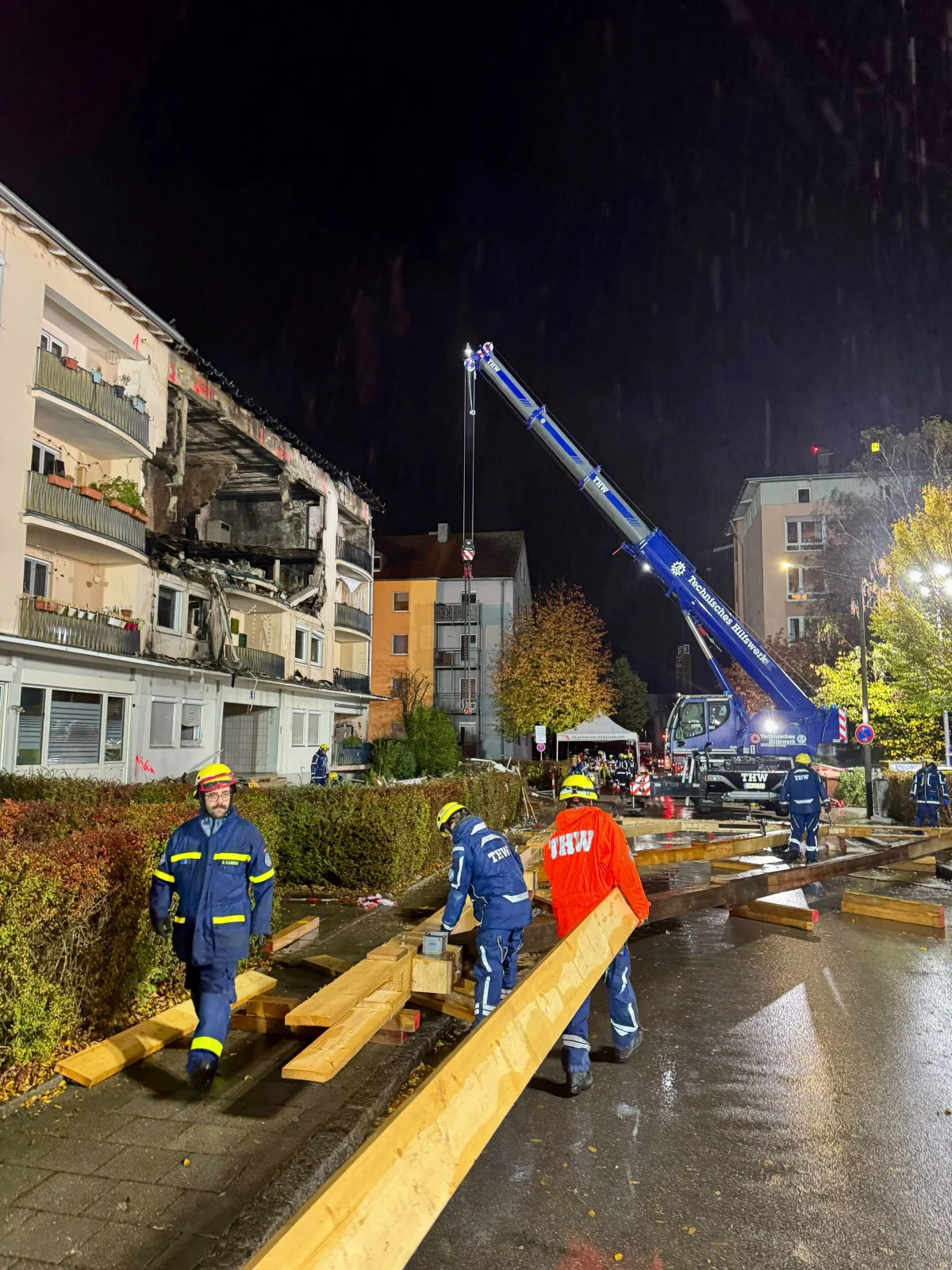 Mehrere THW-Mitarbeiter arbeiten bei Nacht vor einem stark beschädigten Wohnhaus. Ein Kran ist im Einsatz.