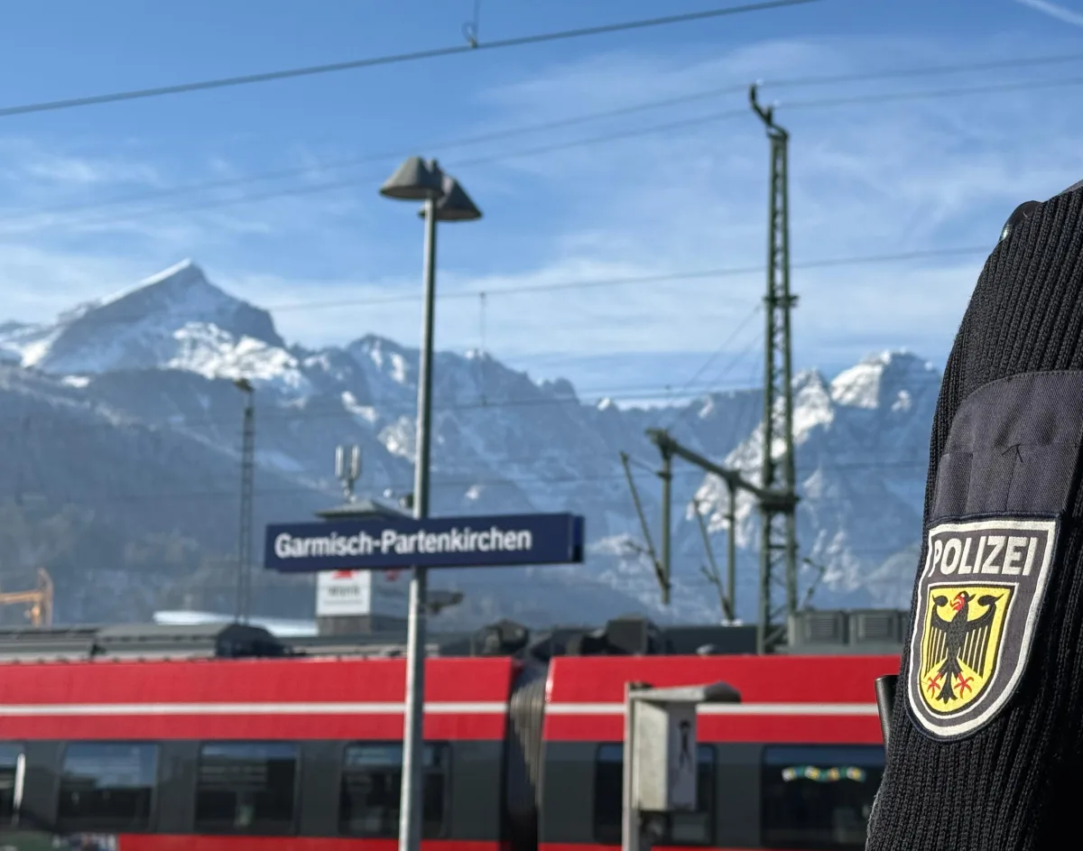 Ein Polizist in Uniform steht am Bahnhof von Garmisch-Partenkirchen. Im Hintergrund sind verschneite Berge sichtbar.