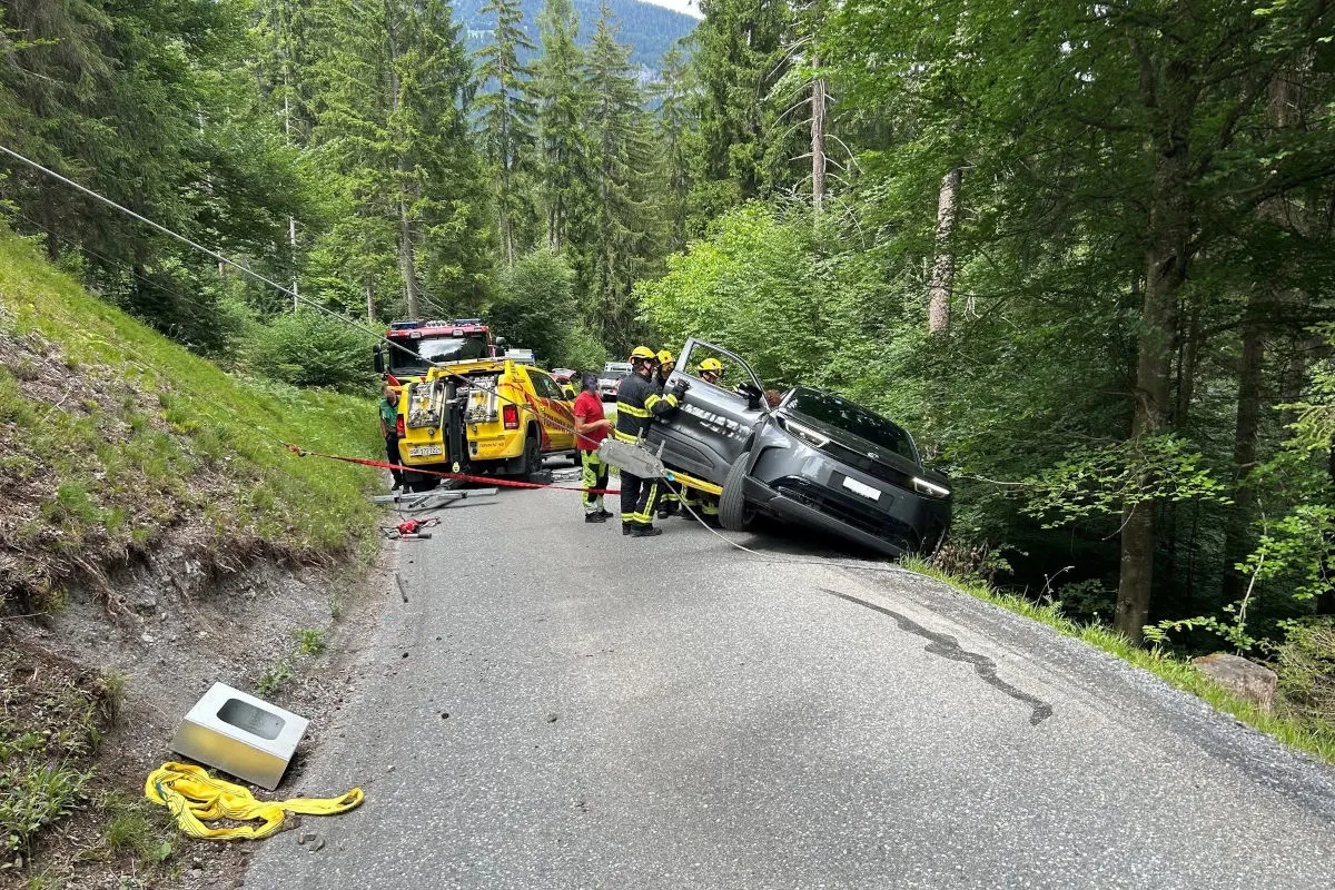 Ein graues Auto ist auf einer schmalen Waldstraße seitlich abgerutscht. Feuerwehrleute und ein gelbes Einsatzfahrzeug sind vor Ort.
