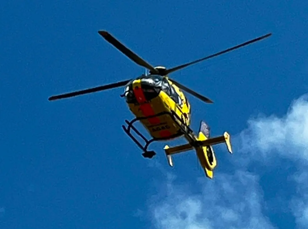 Ein gelber Rettungshubschrauber fliegt am klaren, blauen Himmel. Das Wort 'ADAC' ist auf der Unterseite sichtbar.