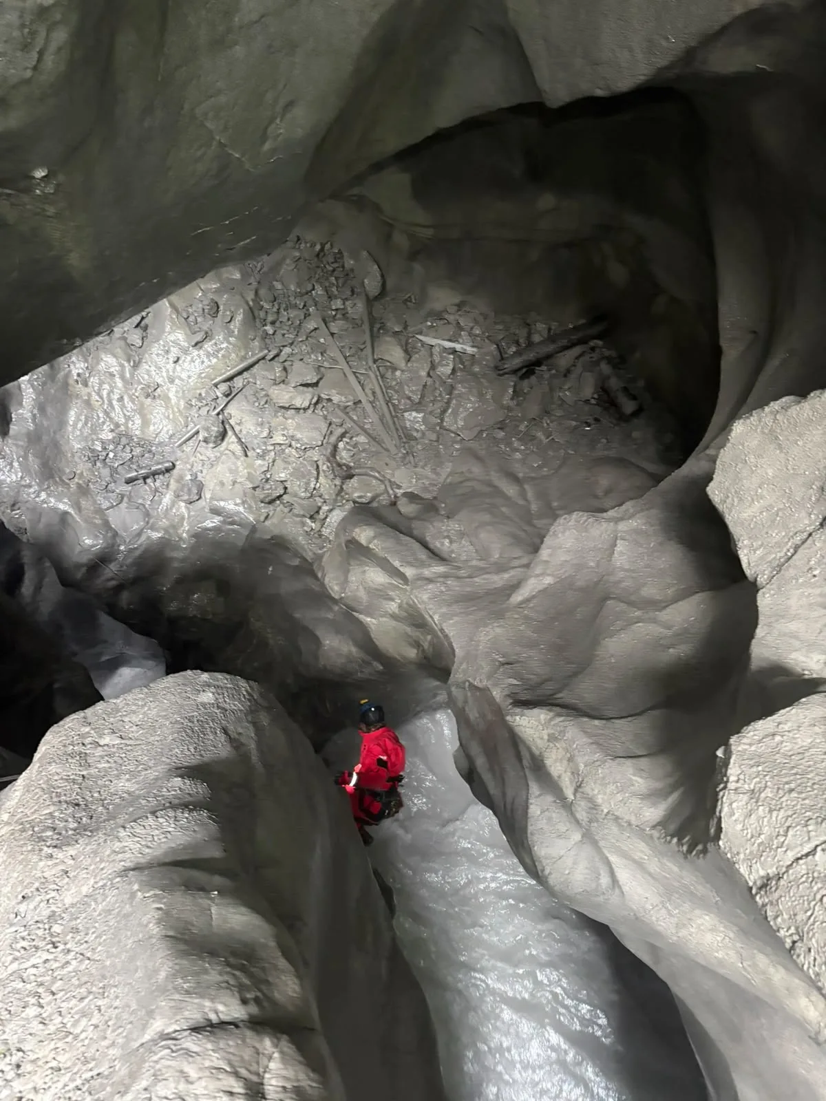 Eine Person in einem roten Schutzanzug steht in einer felsigen Höhle und untersucht die Umgebung.