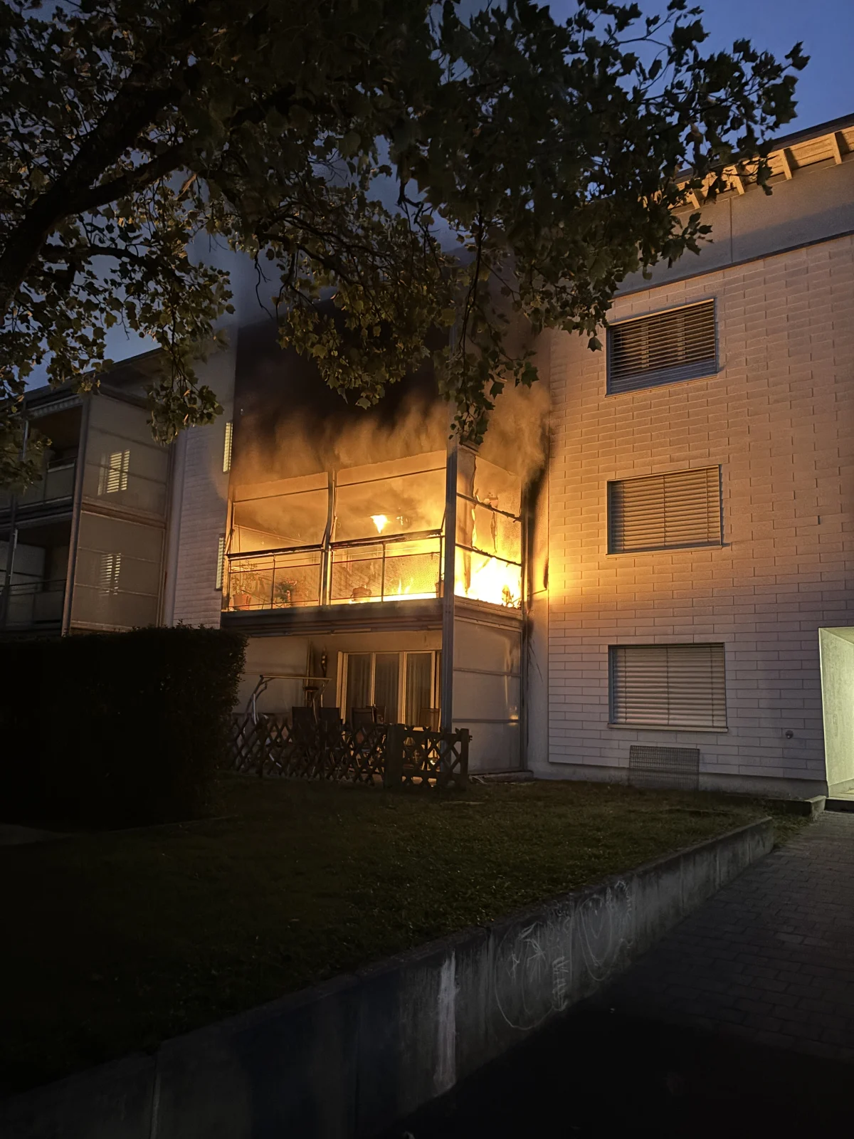 Ein Balkon eines mehrstöckigen Wohnhauses steht in Flammen. Dunkler Rauch steigt auf, während es draußen dämmert.