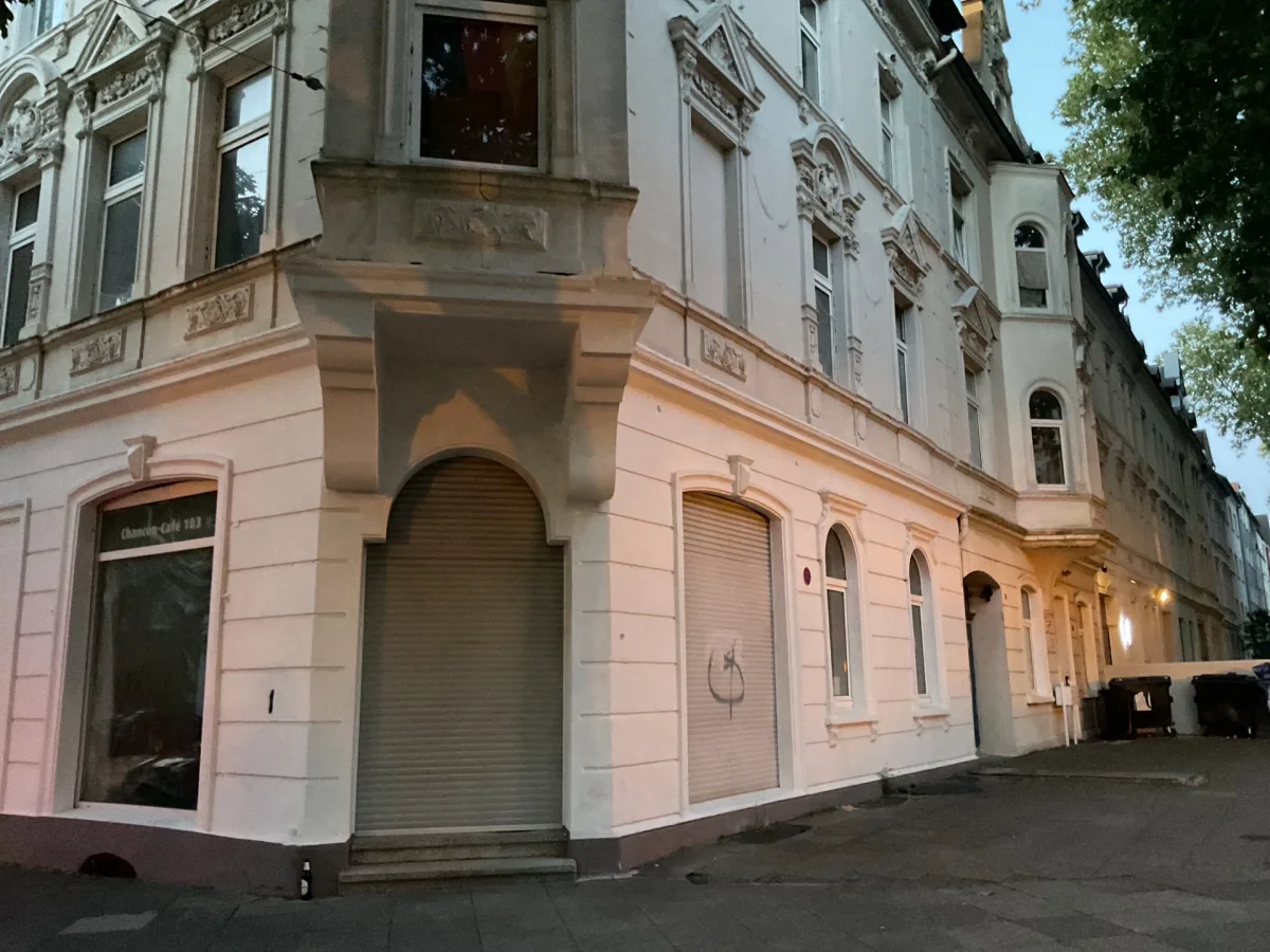 Fassade eines historischen Gebäudes mit detaillierten Verzierungen, auf dem Bürgersteig steht eine leere Flasche.