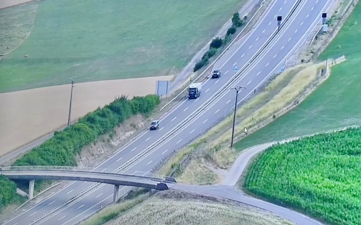Aus der Vogelperspektive sichtbare Landstraße mit einem LKW und mehreren Pkw auf einer zweispurigen Fahrbahn, umgeben von Feldern.