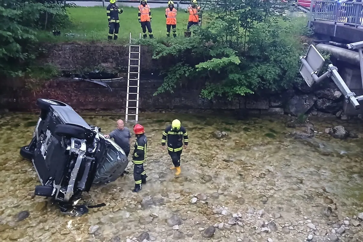 In einem flachen Bachbett liegt ein umgekippter Wagen. Feuerwehrleute stehen um das Fahrzeug herum und sichern die Szene. Eine Leiter führt die Böschung hinauf.