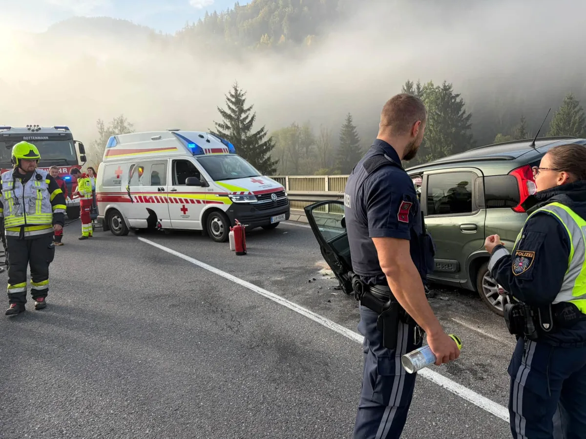 Mehrere Einsatzkräfte sind an einer Unfallstelle auf einer Straße; im Hintergrund dichter Nebel und ein Rettungswagen.