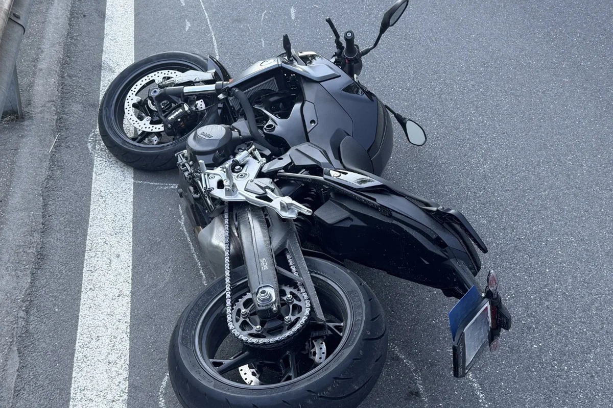 Ein schwarzes Motorrad liegt seitlich auf einer asphaltierten Straße nahe einer Leitplanke. Die Straße zeigt Fahrbahnmarkierungen an der Seite.