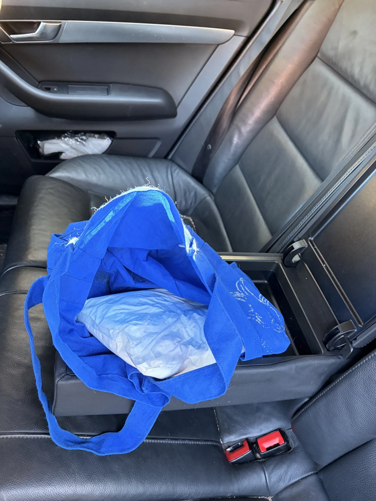 Eine blaue Stofftasche liegt geöffnet auf dem schwarzen Rücksitz eines Autos. Im Inneren ist ein weißes Bündel sichtbar.