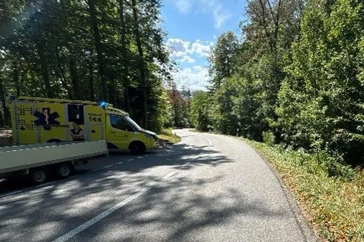 Ein gelber Krankenwagen steht quer auf einer kurvigen Straße im Wald. Die Sonne scheint durch die Bäume.