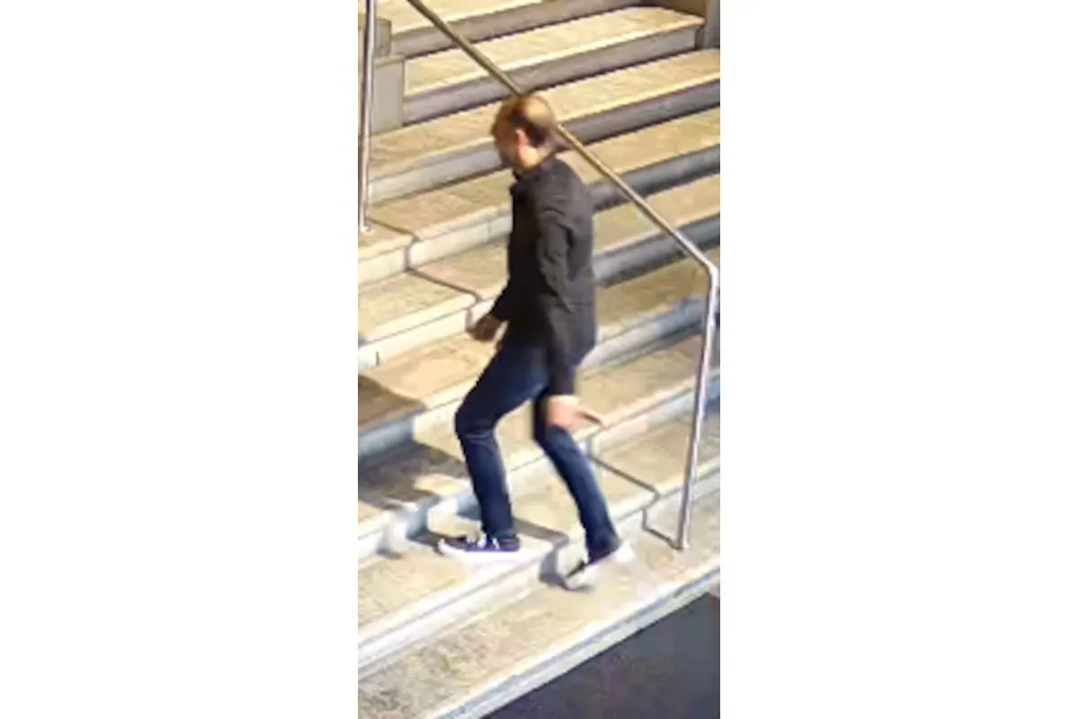 Ein Mann in dunkler Kleidung steigt in einem Gebäude eine breite Treppe hinauf. Die Szene wirkt modern beleuchtet.