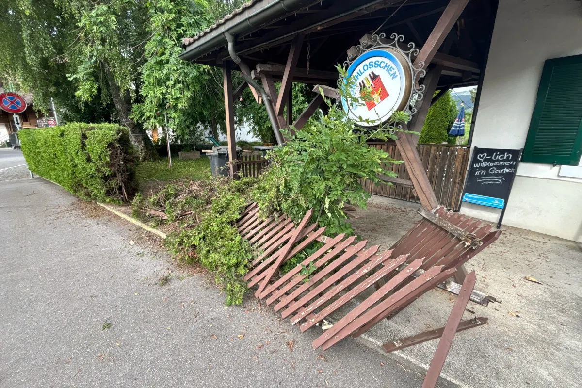 Ein Holzzaun ist teilweise umgefallen und beschädigt, vor einem Gasthaus mit einem runden Schild.
