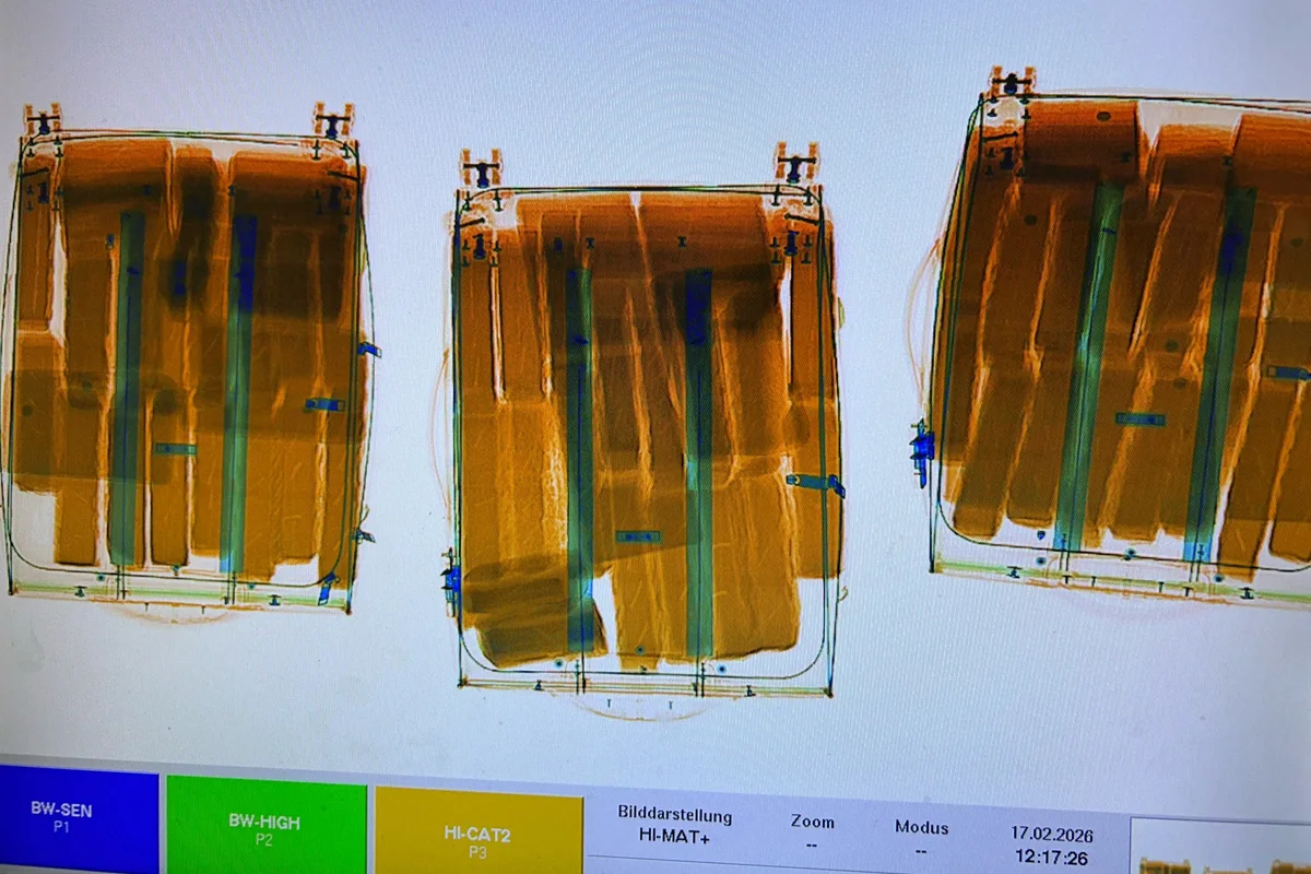Die Aufnahme zeigt drei Röntgenbilder von Koffern, die nebeneinander auf einem Monitor dargestellt sind. Die Bilder wirken dreidimensional und zeigen innere Strukturen der Koffer. Unten auf dem Bildschirm sind Menüelemente und ein Datum sichtbar.