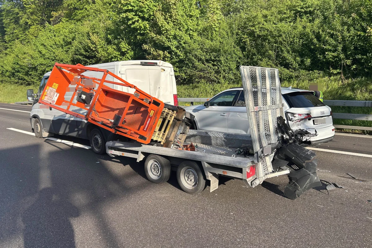 Ein Anhänger mit einem beschädigten Aufbau steht auf der Autobahn. Im Hintergrund ist ein weißes Auto zu sehen.