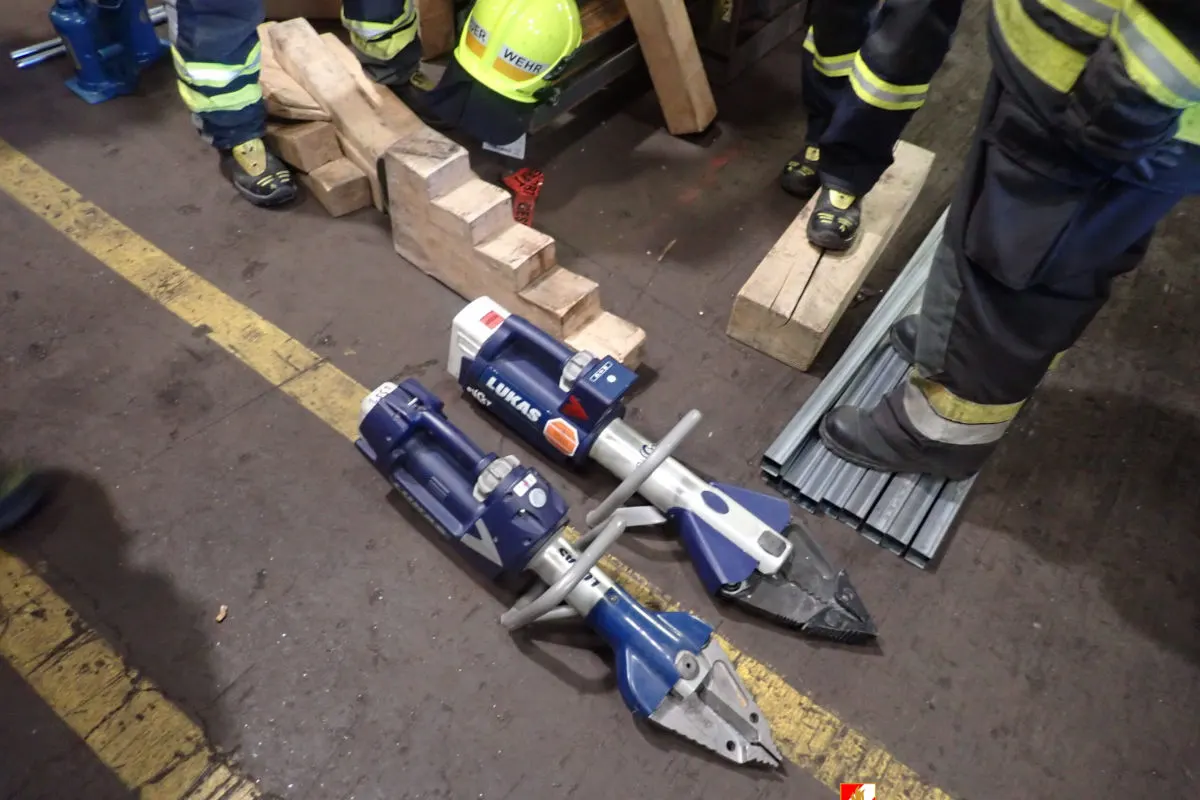 Ein Satz hydraulischer Rettungsgeräte liegt auf einem Hallenboden, umgeben von Holzblöcken und Schuhen von Einsatzkräften.