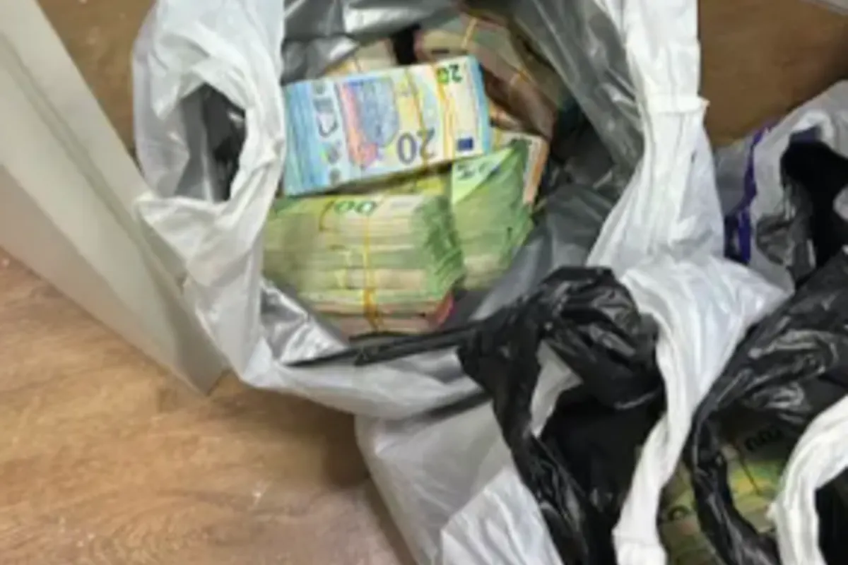 Mehrere Plastiksäcke, die mit gestapelten Euroscheinen gefüllt sind, liegen offen auf einem Holzboden. Die Scheine sind als 20- und 100-Euro-Noten erkennbar.