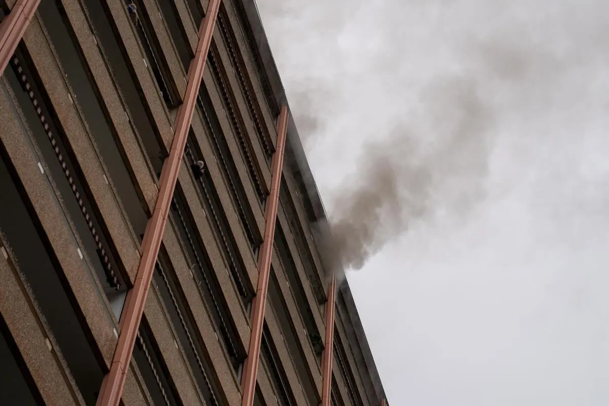 Ein mehrstöckiges Gebäude mit dichtem Rauch, der aus einem Fenster in den grauen Himmel strömt, ist sichtbar.