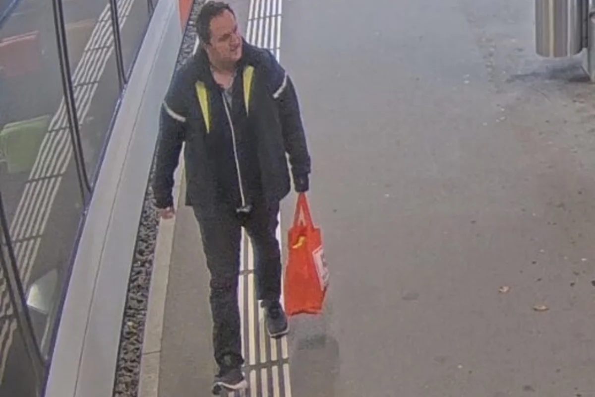 Eine Person geht auf einem Bahnsteig entlang und trägt eine rote Einkaufstasche. Rechts ist ein Zug zu sehen.