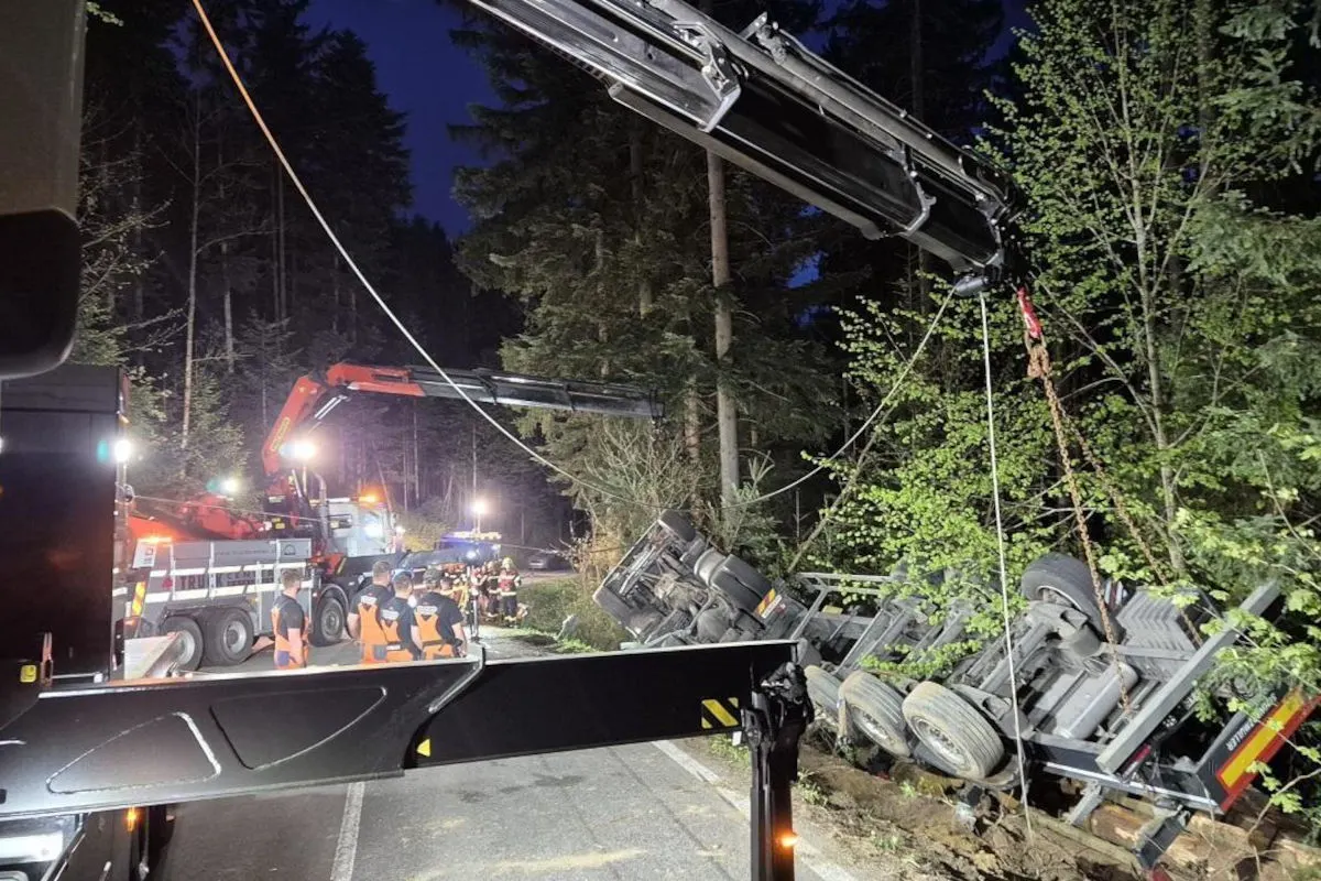 In einem Waldgebiet wird bei Nacht ein Lastwagen von zwei Kränen angehoben. Mehrere Einsatzkräfte mit Warnwesten sind vor Ort.