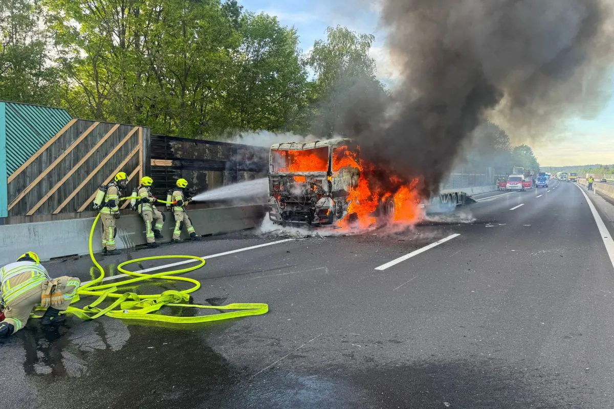 Auf einer Autobahn löscht die Feuerwehr einen brennenden LKW. Dichter Rauch steigt aus dem Fahrzeug auf.