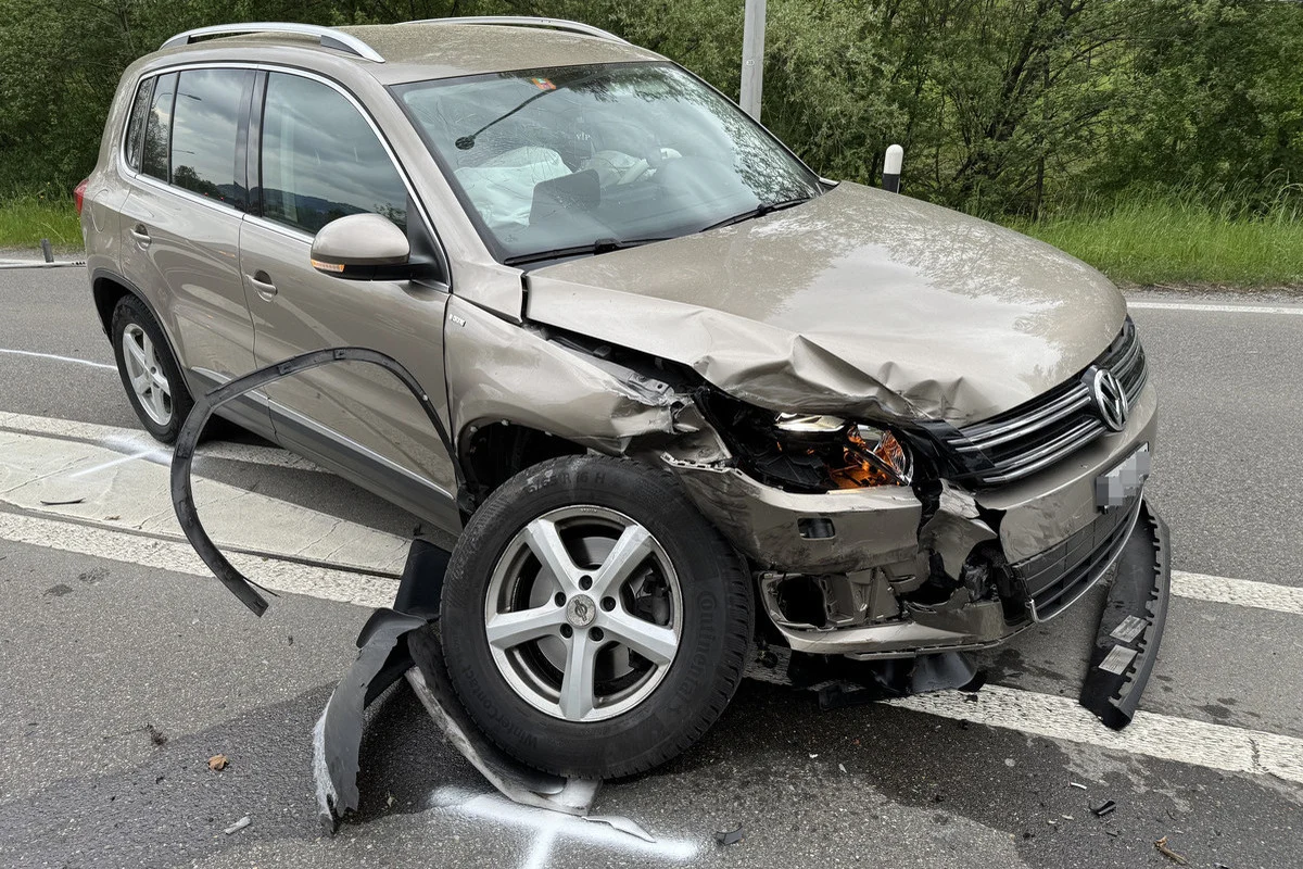 Ein silbernes Auto mit deutlichem Frontschaden steht auf einer Straße. Teile der Stoßstange liegen auf dem Boden.