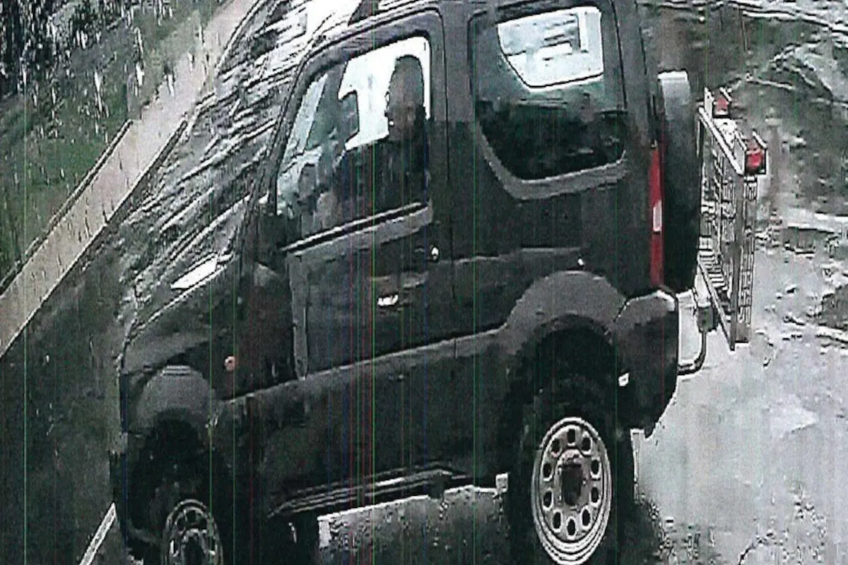 Ein schwarzes, kompaktes Fahrzeug steht auf einer nassen Straße. Der Fahrer ist durch die nasse Fensterscheibe sichtbar.