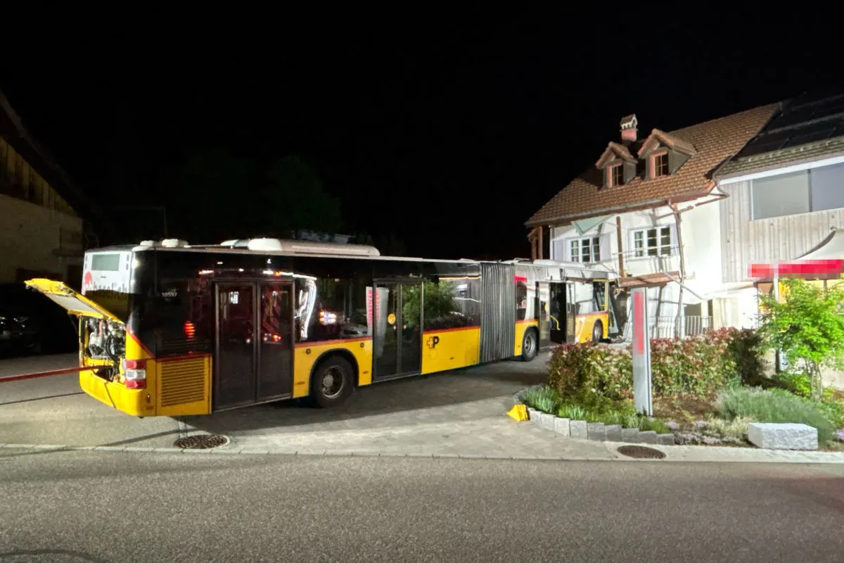 Ein gelber Postauto-Bus ist in der Nacht gegen ein Gebäude gefahren. Der Bus ist beschädigt, und die Fassade des Gebäudes zeigt Spuren des Aufpralls.