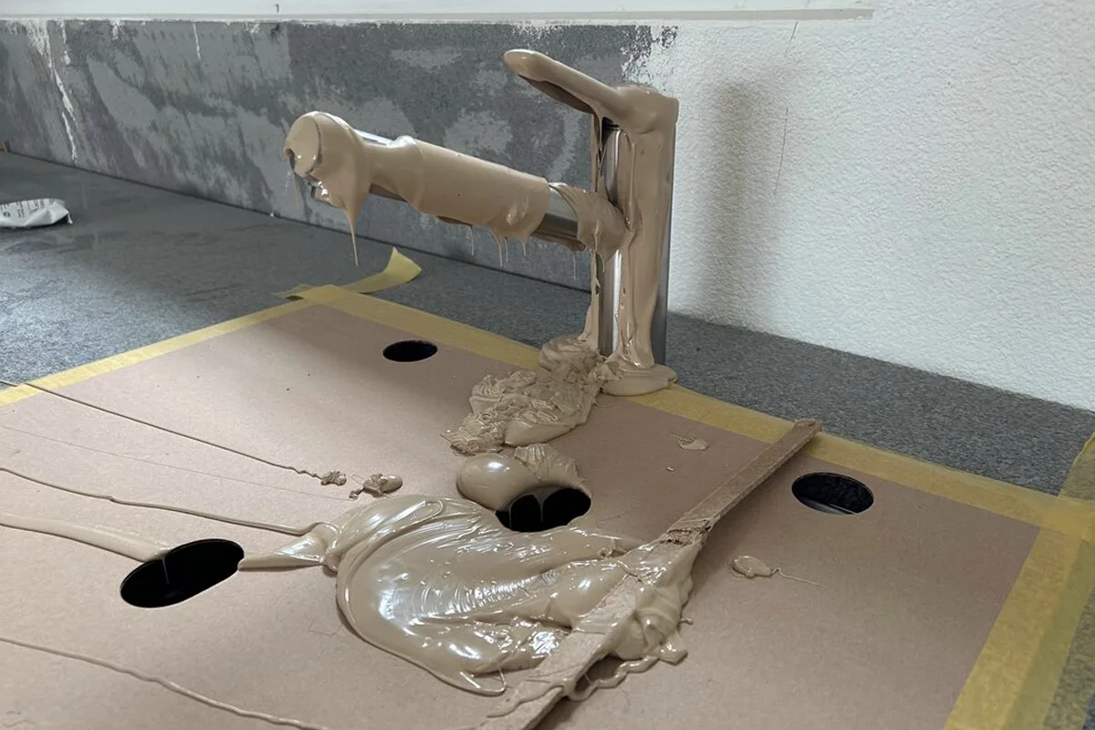 Ein verchromter Wasserhahn ist vollständig mit Bauschaum bedeckt. Der Schaum hat sich über eine Abdeckung aus Papplage verteilt.