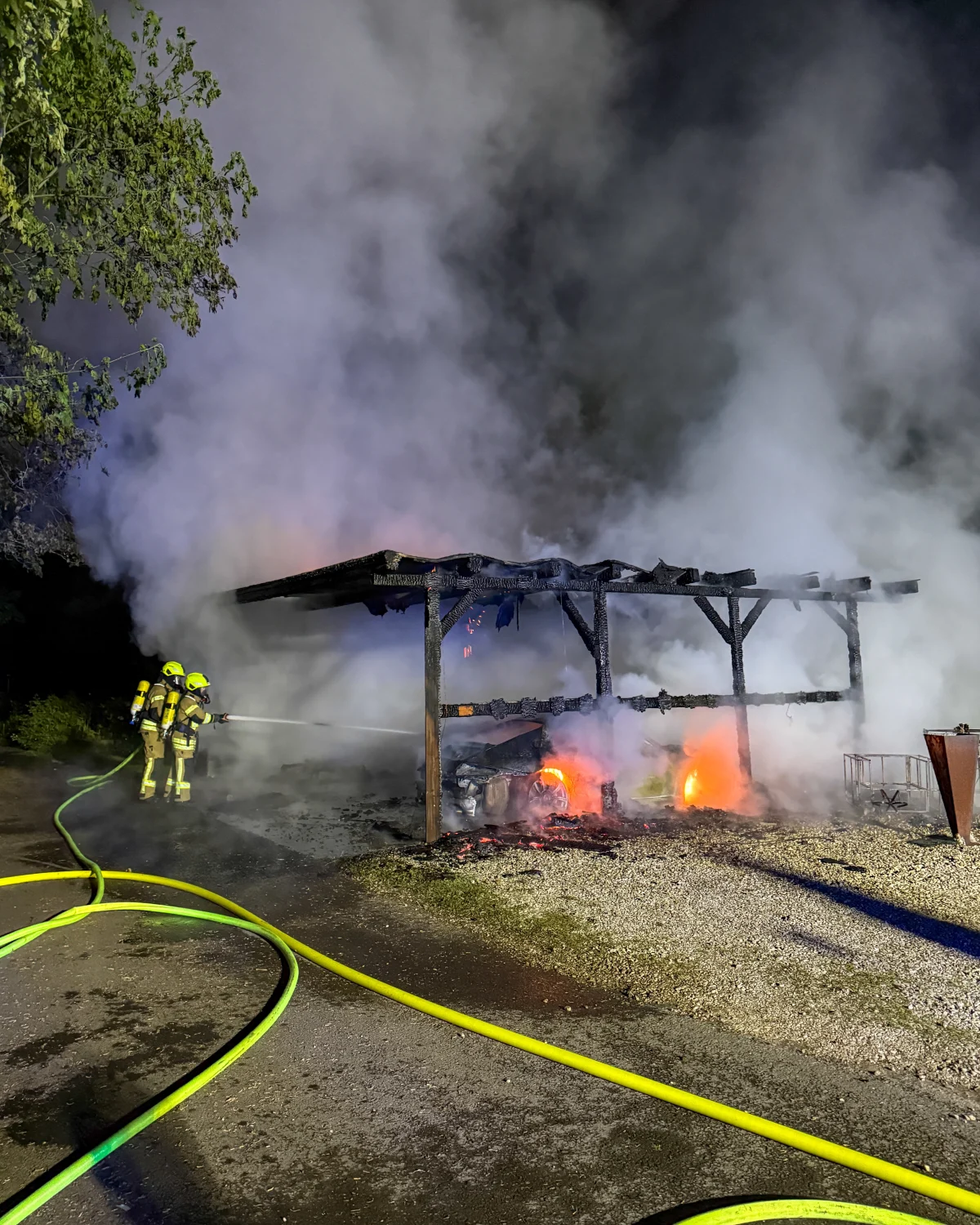 Zwei Feuerwehrmänner bekämpfen nachts einen Brand an einem Schuppen, aus dem Rauch aufsteigt.