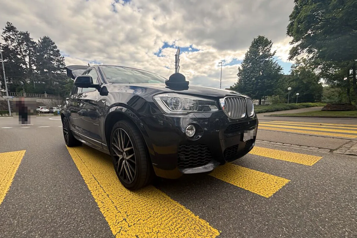 Ein schwarzer BMW steht auf einem Zebrastreifen, die Motorhaube ist leicht geöffnet. Der Himmel ist bewölkt.