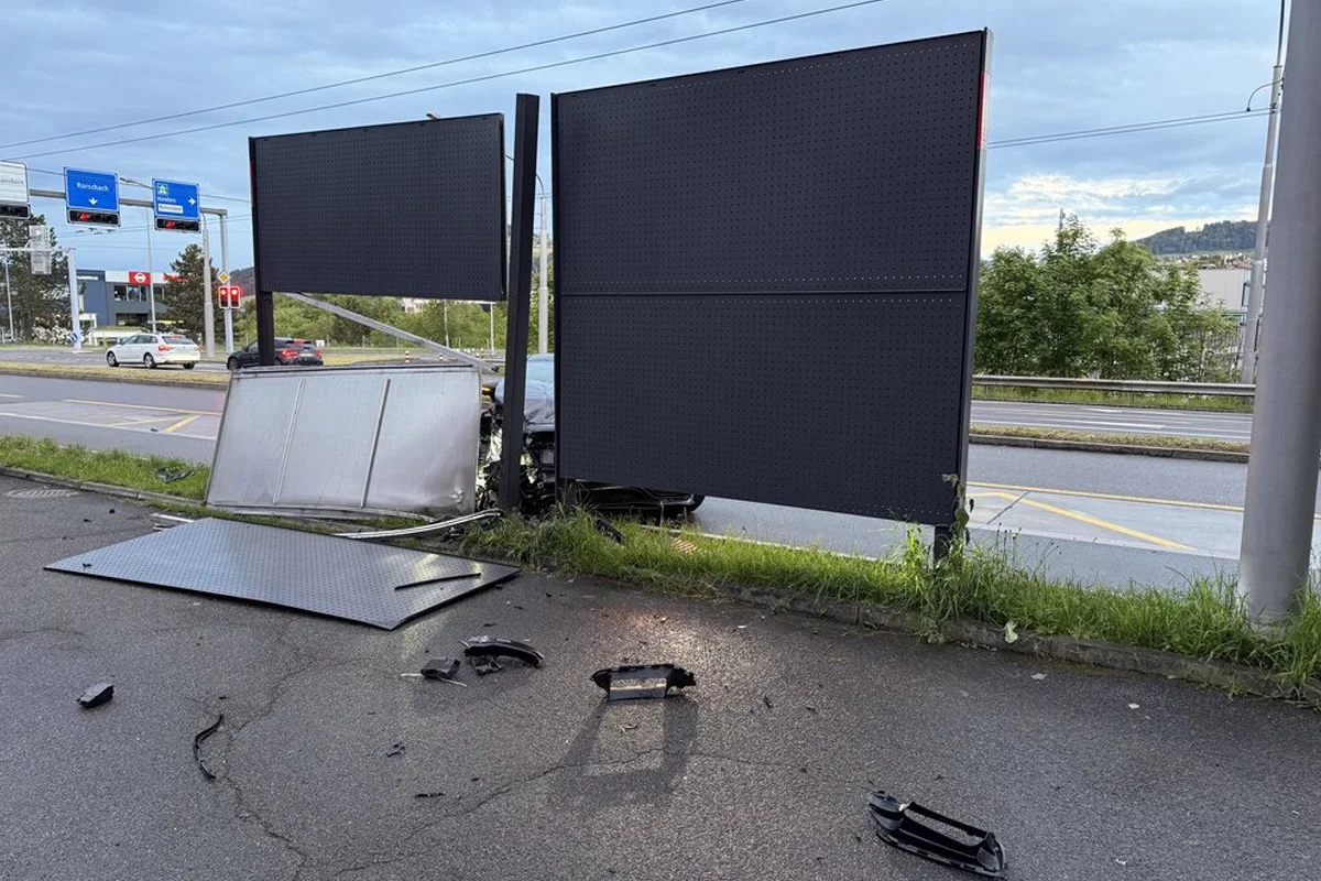 Ein beschädigtes Verkehrsschild liegt neben der Straße, umgeben von verstreuten Trümmerteilen. Im Hintergrund sind eine Stadtkulisse und vorbeifahrende Autos zu sehen.