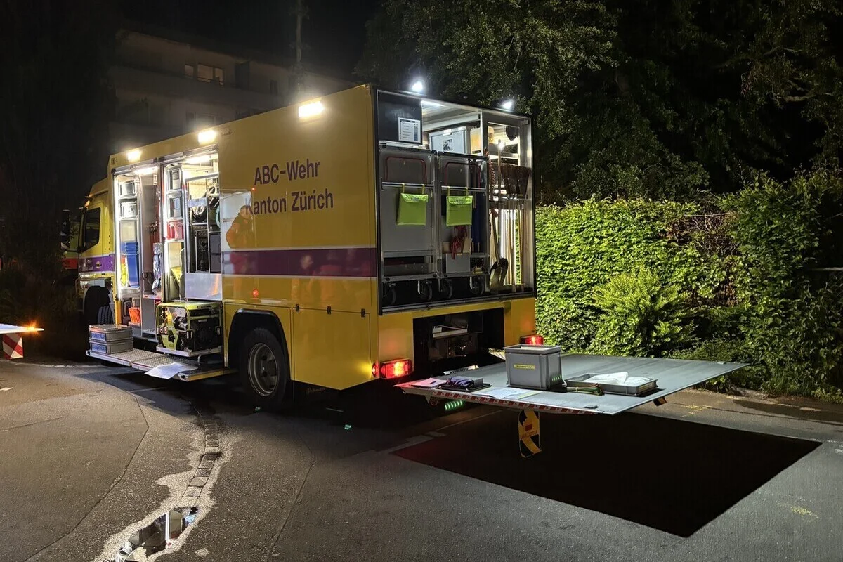 Ein gelbes Einsatzfahrzeug der ABC-Wehr des Kantons Zürich steht bei Nacht mit geöffneter Ladefläche und sichtbaren Ausrüstungsgegenständen auf einer Straße. Im Hintergrund sind Büsche zu sehen.