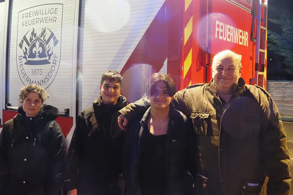 Vier Personen stehen lächelnd vor einem roten Feuerwehrfahrzeug der Freiwilligen Feuerwehr Biedermannsdorf. Das Fahrzeug zeigt das Wappen und die Aufschrift der Feuerwehr.