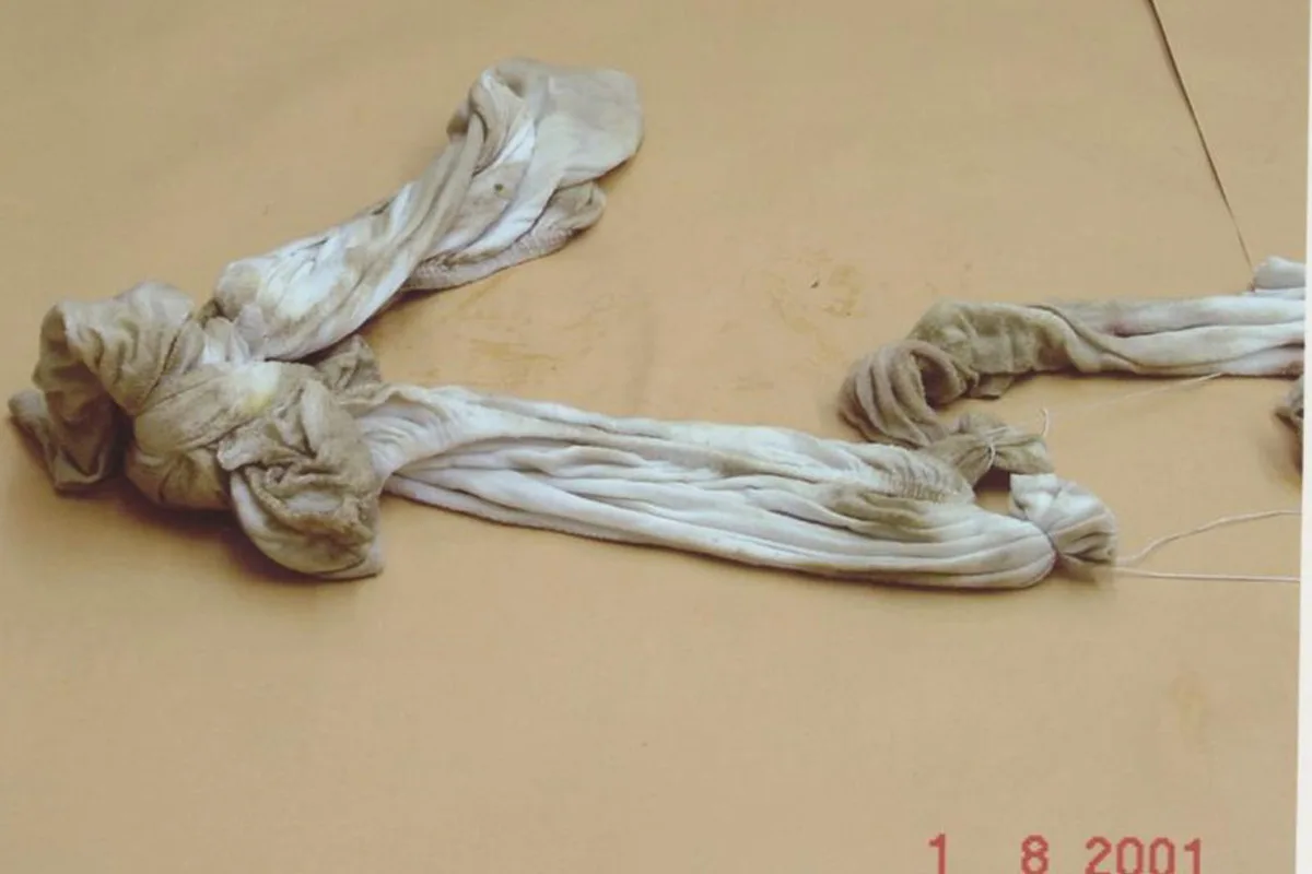 Ein verschmutztes und verknotetes Textil, das auf einem hellen Untergrund liegt. Es wirkt alt und benutzt.