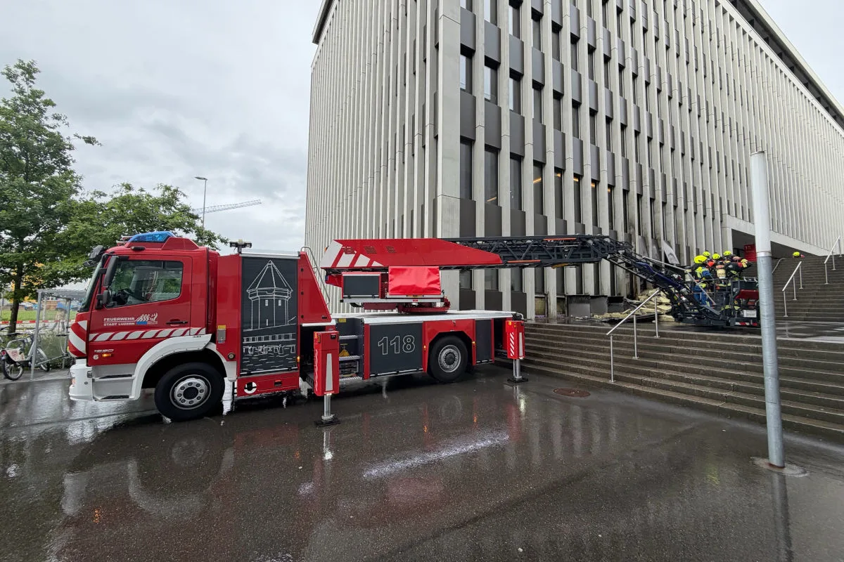 Ein rotes Feuerwehrfahrzeug steht mit ausgefahrener Leiter vor einem großen Bürogebäude. Einsatzkräfte befinden sich auf der Leiter.