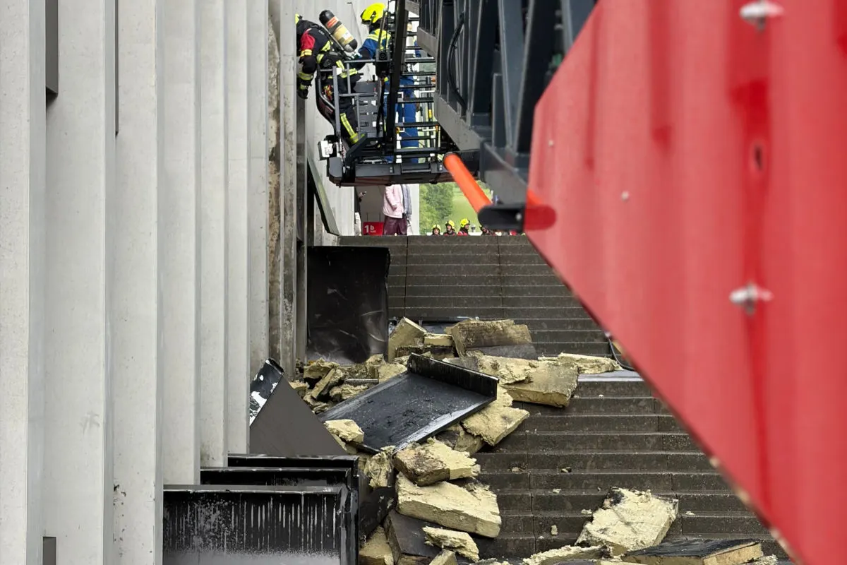 Mehrere Rettungskräfte befinden sich auf einer Hebebühne neben einer zerstörten Gebäudeaußenwand, mit Trümmern am Boden.