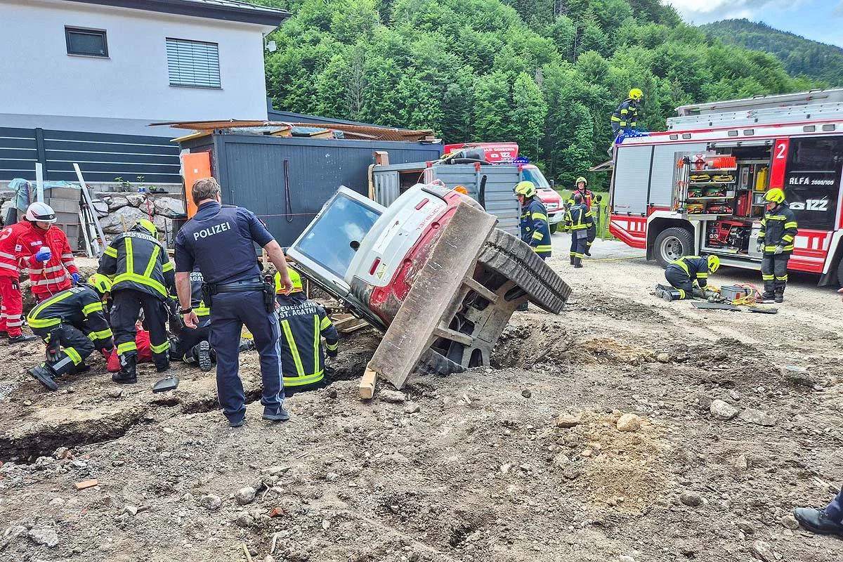 Polizei und Feuerwehr arbeiten an einem umgestürzten Fahrzeug auf einer Baustelle neben einem Gebäude. Mehrere Einsatzkräfte sind beschäftigt.