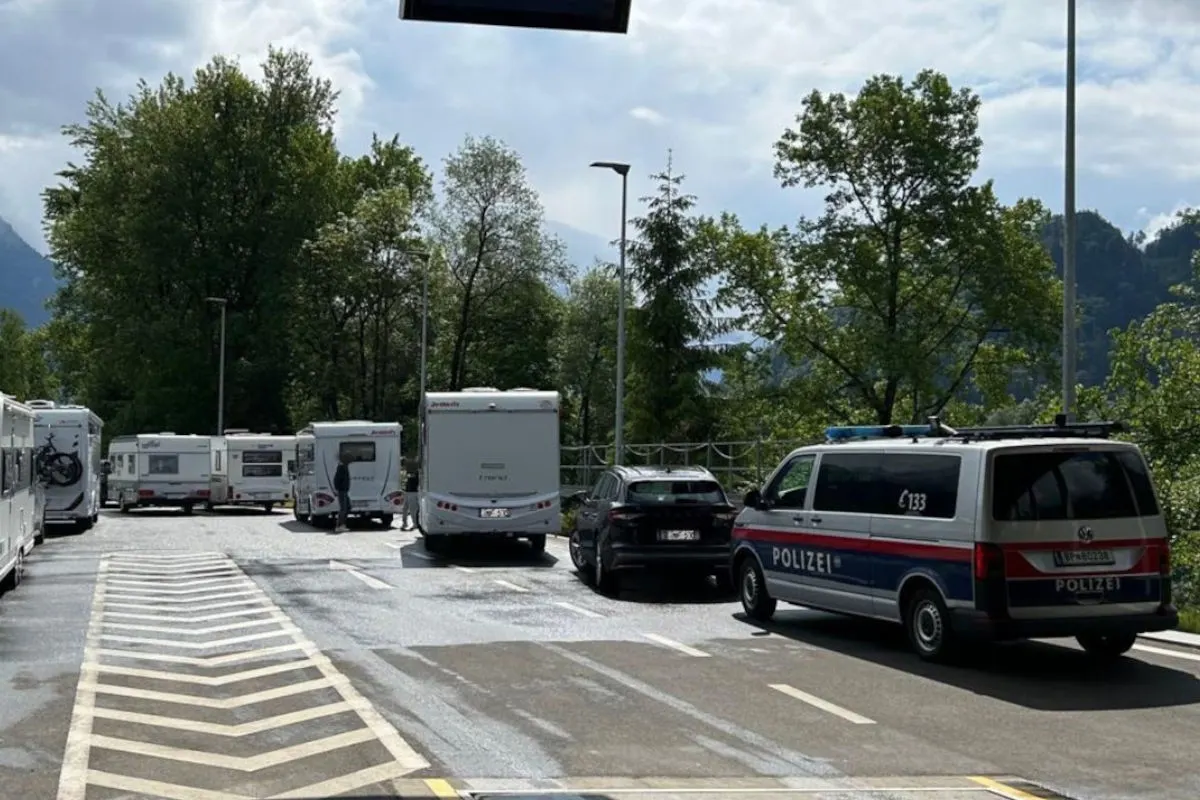 Ein Polizeifahrzeug steht auf einem Rastplatz, umgeben von mehreren Wohnmobilen. Im Hintergrund sind Bäume und Berge zu sehen.