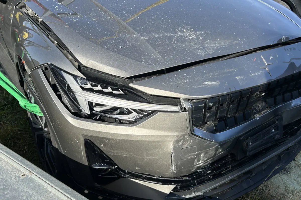 Das Bild zeigt die Front eines grauen Autos mit erheblichen Beschädigungen, wahrscheinlich nach einem Unfall. Der Lack ist zerkratzt, und die Stoßstange ist eingedrückt.
