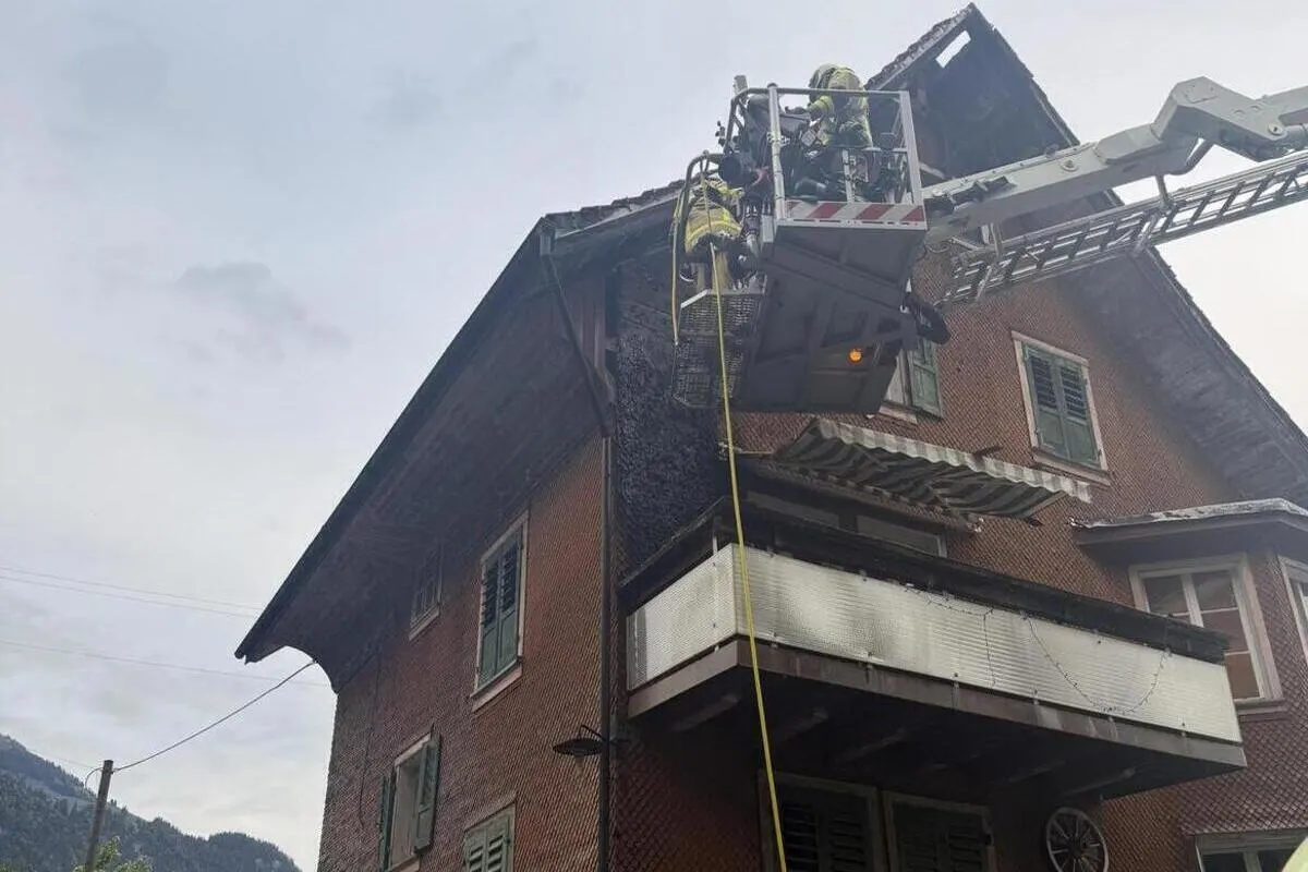Zwei Feuerwehrleute befinden sich in einem Hubrettungsfahrzeug und löschen ein Feuer an der Dachkante eines mehrstöckigen Hauses.