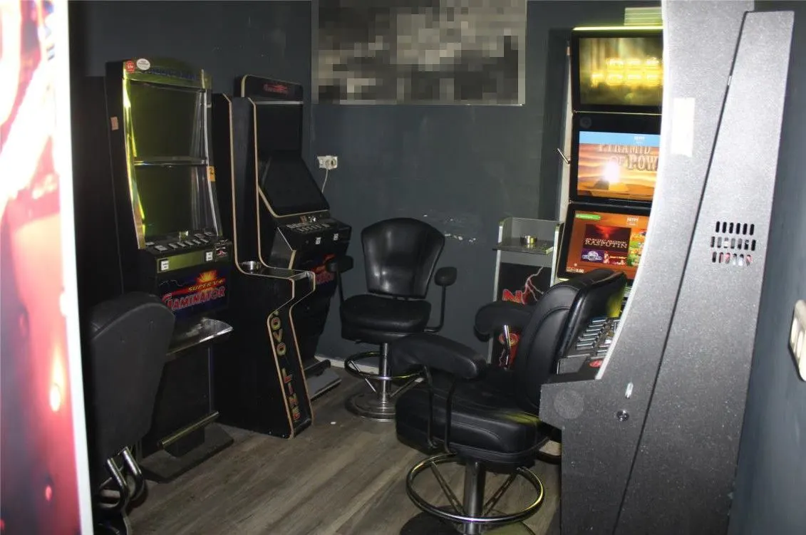 Ein Raum mit mehreren Spielautomaten und schwarzen Lederstühlen. Der Boden ist aus hellem Holz oder Laminat.