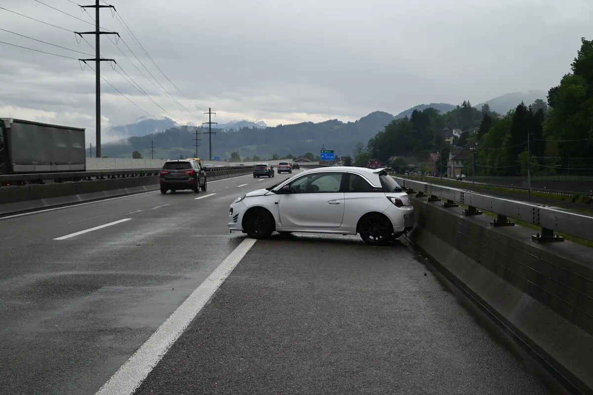 Ein weißes Auto steht quer auf der Autobahn und hat die rechte Leitplanke touchiert. Die Straße ist nass und der Himmel bewölkt.