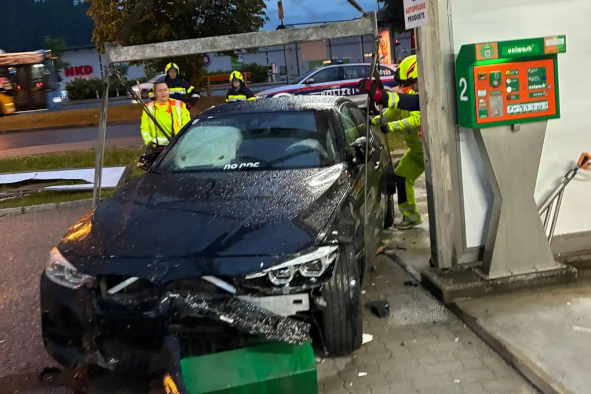 Ein schwarzes Auto mit erheblichen Schäden steht nahe einer Waschanlage. Einsatzkräfte sind um das Fahrzeug versammelt. Es scheint dämmerig zu sein.